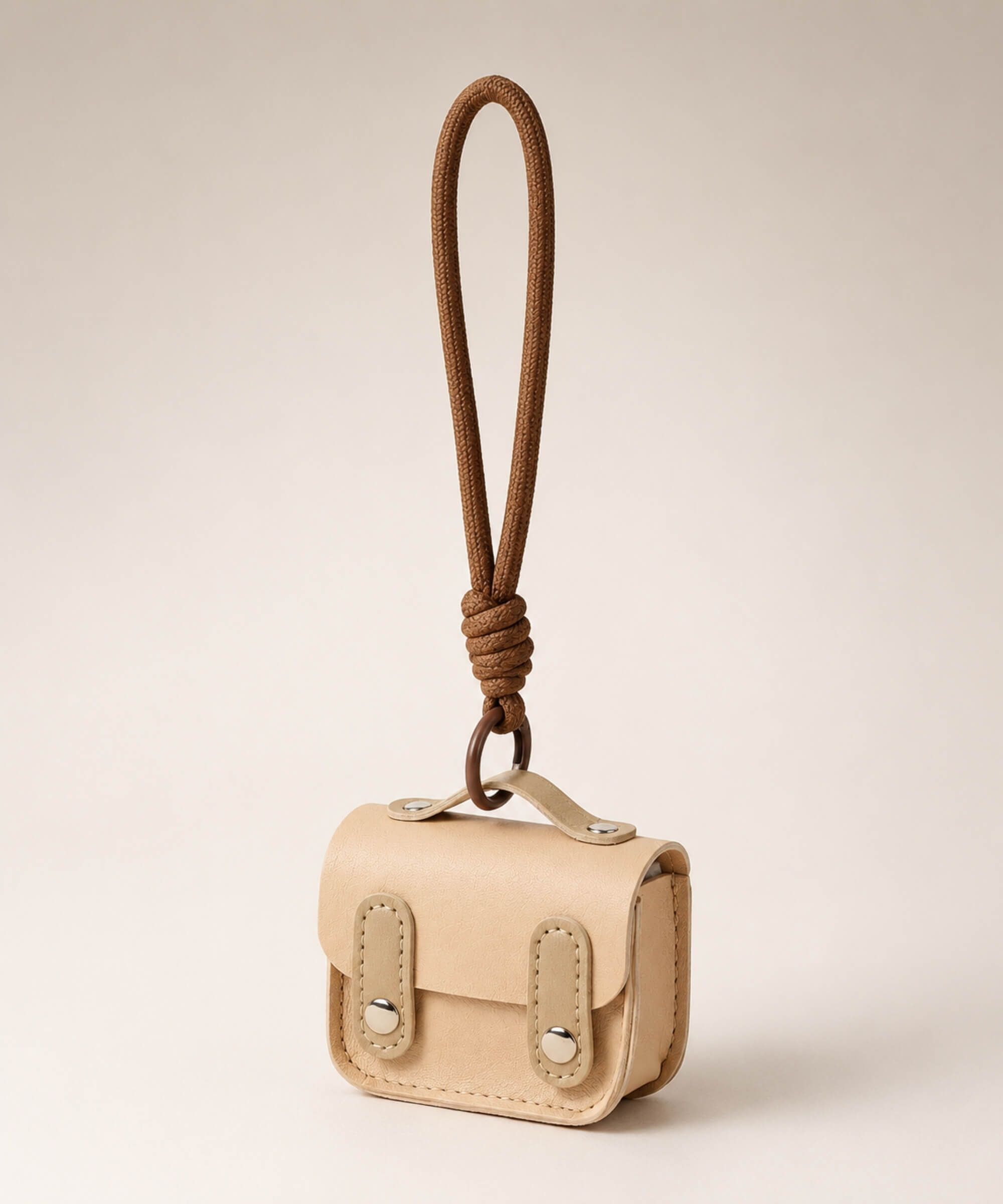 Beige mini PU leather earphone pouch keychain with brown wrist strap on a neutral background